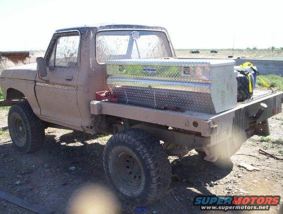Mud-covered flatbed truck with a diamond plate toolbox and spare tire in the bed
