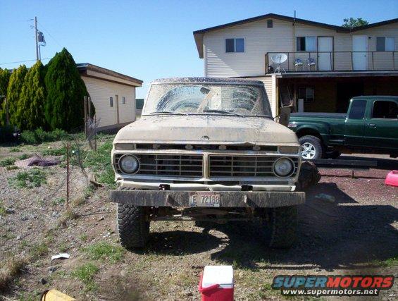 Dusty tan Ford F-Series truck parked in front of a house, with a green pickup truck behind it
