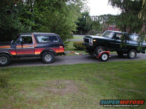 1978 Ford Bronco towing a 1979 Ford Bronco on a trailer. Both vehicles are dark colored