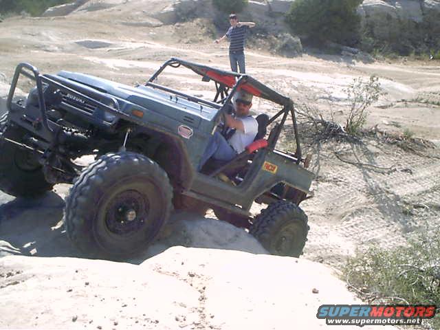 Green off-road vehicle with large tires navigating rocky terrain