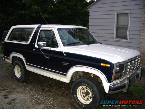 1984 Ford Bronco, two-tone blue and white, parked in gravel driveway next to house