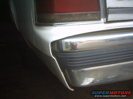 Rear corner of a white car showing a chrome bumper with black rubber trim and a red taillight