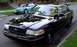 1998 Ford Crown Victoria - A black 1998 Ford Crown Victoria is parked on a residential street, with another car visible in the background.