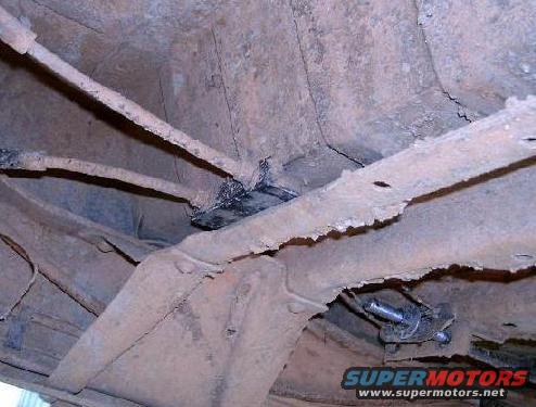 Undercarriage of a heavily rusted vehicle with visible brake lines and frame components