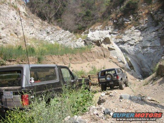1988 Ford Bronco and another SUV on a dirt trail with rocky hillsides