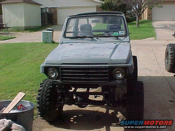 Suzuki Samurai with large tires, lifted suspension, and a gray primer finish. It's parked in a driveway