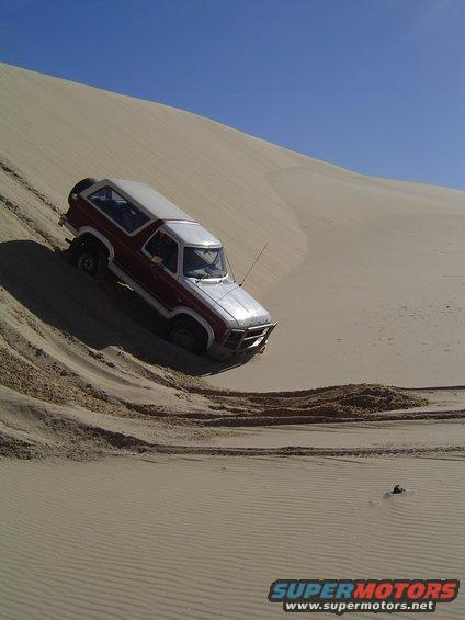 Red and silver Ford Bronco driving on a sand dune