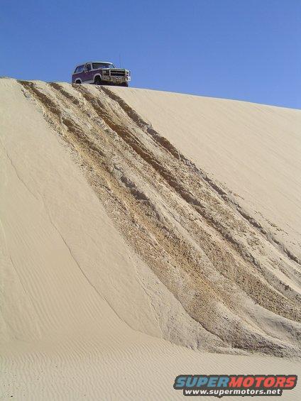1980s Ford Bronco parked on top of a sand dune with tracks leading down