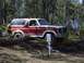 1982 Ford Bronco - A red and white Ford Bronco navigates an off-road course, climbing over fallen trees.