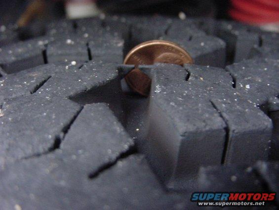 Close-up of tire tread with a penny inserted to show depth