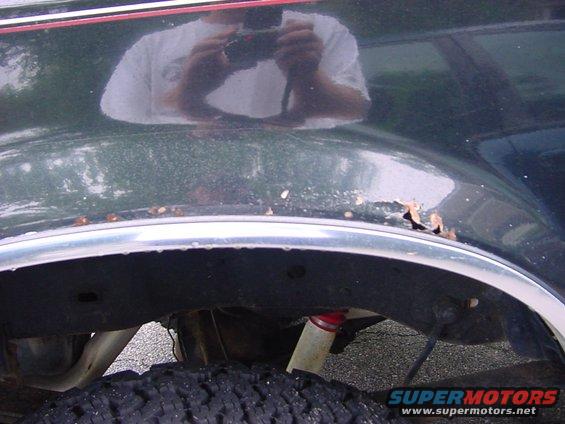 Dark green vehicle fender rust above chrome trim and tire