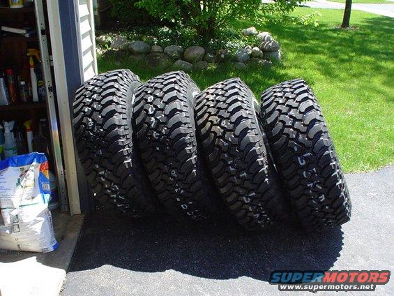 Four large off-road tires leaning against a garage