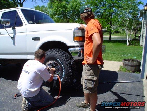 White Ford F-Series truck with large tires, one man inflating a tire while another watches