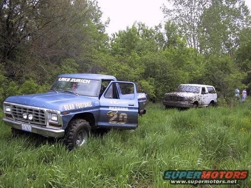 blue pickup truck with 'Lake Zurich' and 'Bear Football' on it, parked next to a muddy white SUV in a grassy field