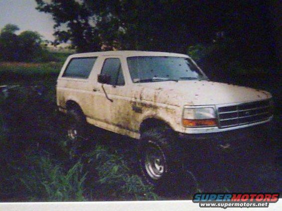 White Ford Bronco covered in mud, parked in tall grass