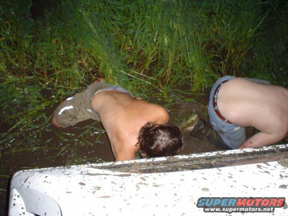 People in mud with a white vehicle part in foreground