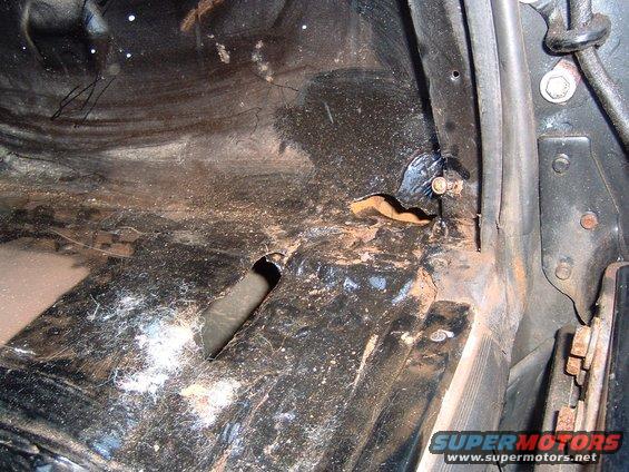 Close-up of a dirty, rusty vehicle floor with a hole and some cobwebs