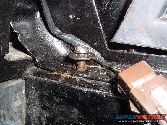 Close-up of a brown electrical connector and a rusted bolt with a washer on a black metal bracket