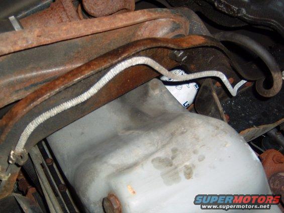 Underside of a vehicle showing a light-colored oil pan with stains and rusty metal components above
