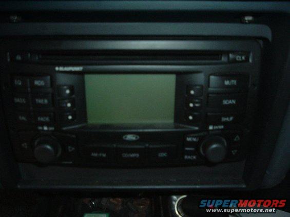 Car stereo with a green display and various buttons, including 'MUTE', 'SCAN', and 'MENU'