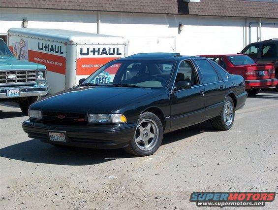Black 1996 Chevrolet Impala parked next to a U-Haul truck and a red Volvo
