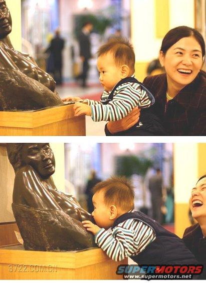 Baby reaching for a statue while a woman laughs behind him