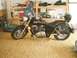 1989 Ford Bronco - A black motorcycle is parked in a garage or workshop, with shelves and storage in the background. The SuperMotors.net logo is visible on th…