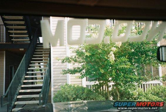 Car interior view through windshield showing reflection of "MOD.COM" text and exterior scene with stairs and building