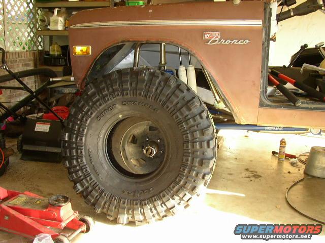 Brown 1974 Ford Bronco with large off-road tire, jack, and lawnmower