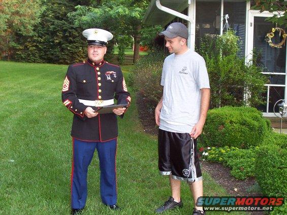 Man in Marine dress uniform stands on grass next to a man in a t-shirt and shorts