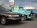 1992 Ford Crown Victoria - A row of vehicles, including a dark sedan and a custom pickup truck with flame graphics, are parked outdoors.