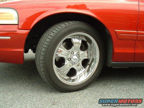 Red sedan's front wheel with chrome rims. The body style suggests a 1998 model