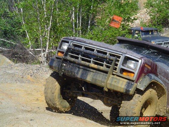 Muddy SUV climbing a dirt hill with another vehicle behind it