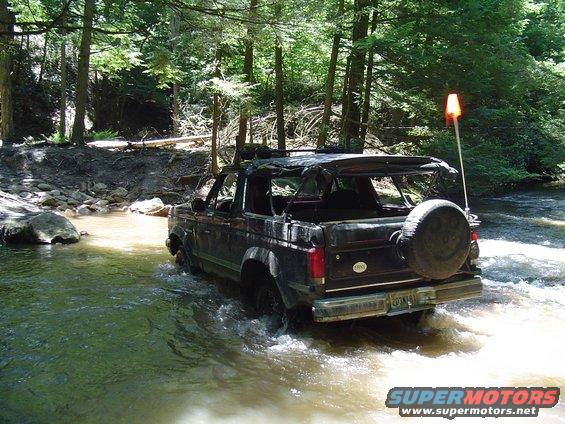 1993 Ford Bronco driving through a forest stream, rear view