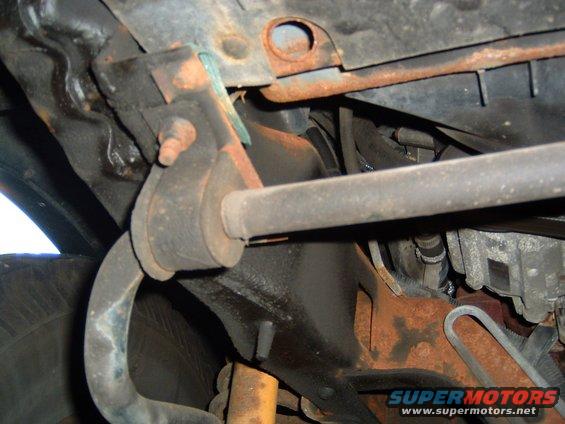 Undercarriage of a vehicle with visible rust on suspension components and a tire in the background