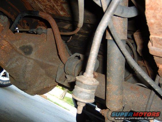 Close-up of rusty rear axle, shock absorber, and sway bar links on a vehicle
