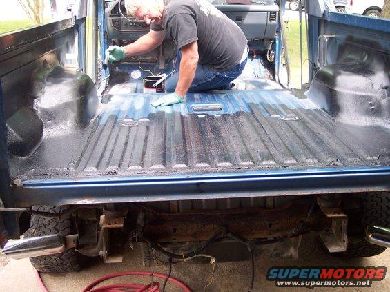 Man applying bedliner inside the bed of a blue 1990 Ford Bronco
