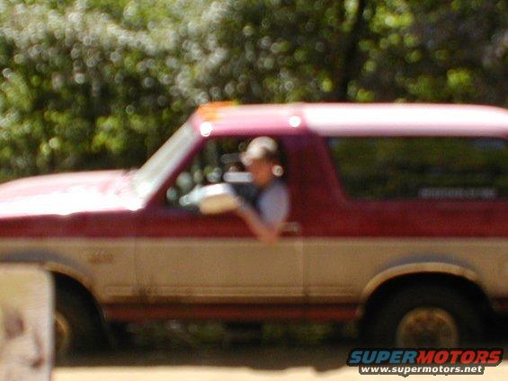 Side view of a red and white two-door SUV, possibly a 1978 Ford Bronco, with a person visible through the driver's window