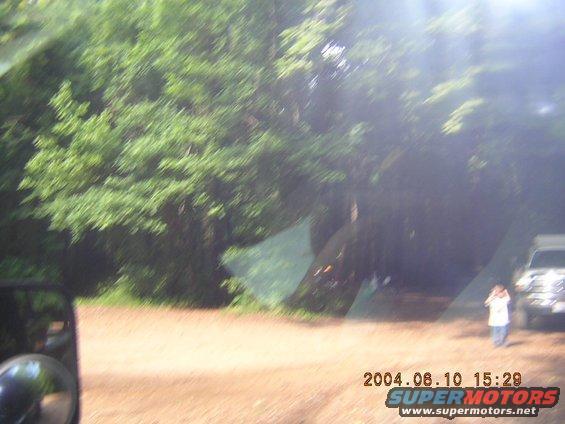 Truck parked on dirt road with trees in background. Person standing nearby