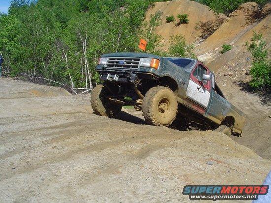 Green and red Ford F-Series truck with large tires climbing a dirt hill