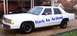 1991 Ford Crown Victoria LTD - A white sedan with blue lettering on its side is parked in a driveway, with another dark vehicle visible behind it.