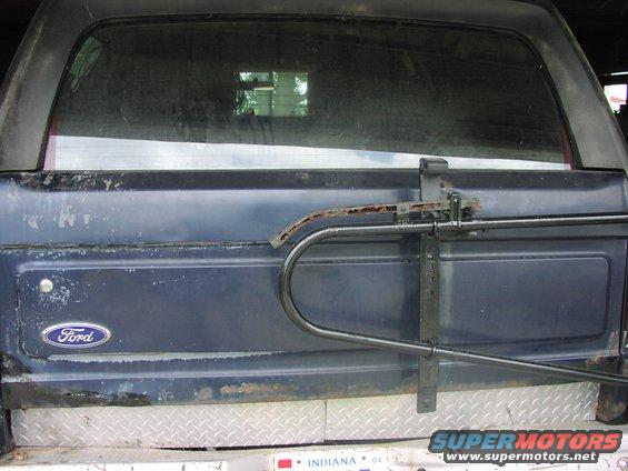 Rear of a dark blue Ford Bronco showing the tailgate and a swing-away spare tire carrier. Ford logo visible on the tailgate