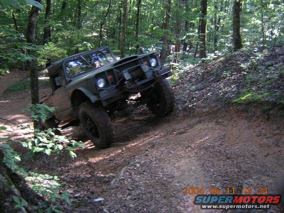 Olive green off-road vehicle climbing a dirt hill in a forest