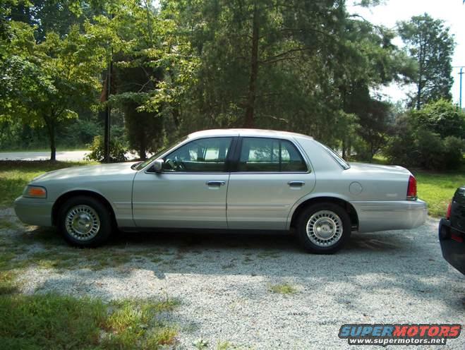 Silver 2000 Ford Crown Victoria parked on a gravel driveway with trees in the background