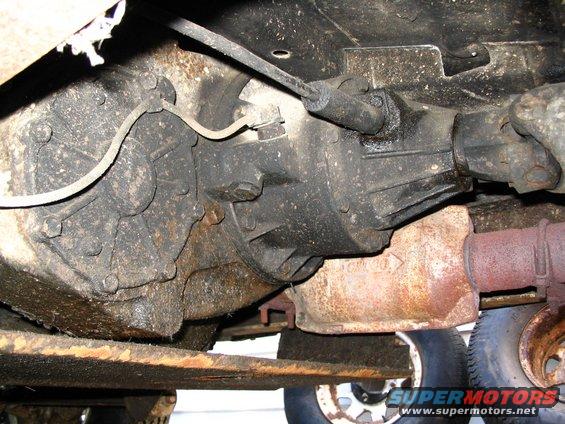 Underside of a vehicle showing the transmission, driveshaft, and part of the exhaust system. Some rust is visible