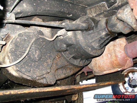 Underside of a vehicle showing a transfer case, exhaust pipe, and part of a wheel