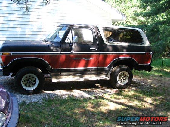 1978 Ford Bronco parked outside, side view. Black and red paint with white wheels
