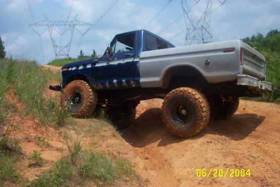 Blue and silver Ford F-150 pickup truck with large off-road tires on a dirt hill