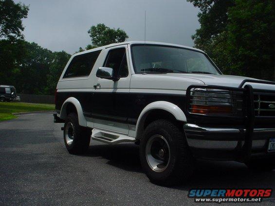 White and black two-door Ford Bronco with a brush guard and running boards, parked on asphalt
