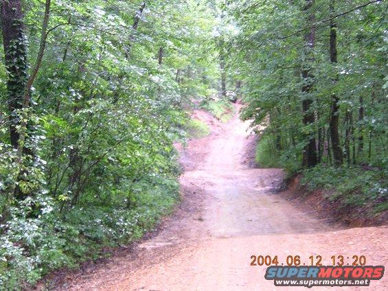 Dirt road going uphill into woods, with a vehicle visible in the distance